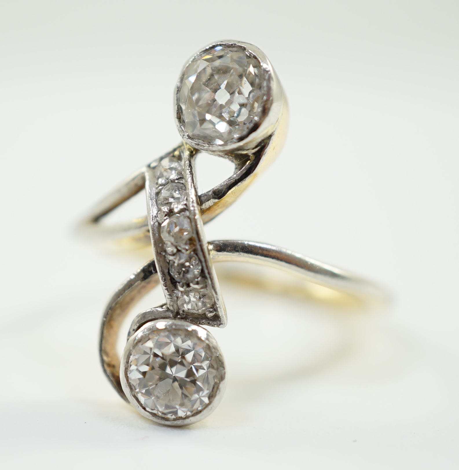 An early to mid 20th century gold and two stone diamond cross over ring, with five stone diamond chip setting